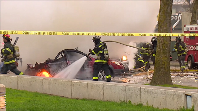 A fireman douses the remaining flames after a KOMO TV helicopter crashed and landed on this car driven by Richard Newman who survived and recovers at Harborview tonight with  his family and his partner at his side. Photo: KOMO TV